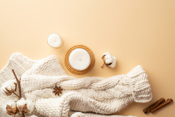 Winter aesthetic concept. Top view photo of knitted pullover candles on rattan serving mat cinnamon sticks anise and cotton branch on isolated beige background