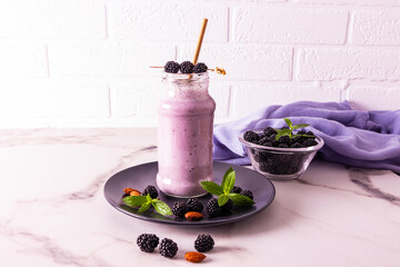 A glass bottle of blackberry smoothie or cocktail stands on a dark ceramic plate on a marble table against a brick wall. healthy eating. diet.
