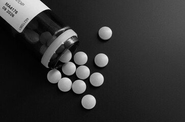 Fototapeta Butelka z rozsypanymi niebieskimi tabletkami leków czarno białe zdjecie obraz
