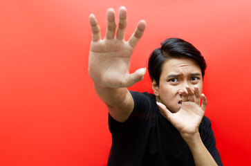 asian man making frightened gestures with his palms as if trying to defend himself from someone while having a terrified expression on his face.