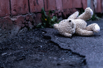 Teddy bear toy lies outdoors on dirty road as symbol of children's loneliness, pain, loss childhood...