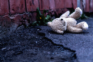 Teddy bear toy lies outdoors on dirty road as symbol of children's loneliness, pain, loss childhood and future. Copy space for text or design.