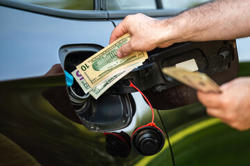 hand of man that puts money into the tank of car, close up, concept of expensive fuel, fuel crisis