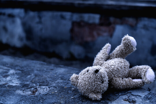 Dirty teddy bear toy lies outdoors on the road as symbol of children's loneliness, pain, loss childhood and future.  Horizontal image. Copyspace for tex or design.