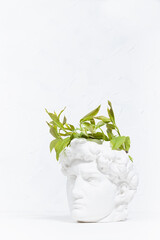 Idea concept with head of white antique statue David and abstract image of his thinking process as young spring green leaves grow of head as thoughts. Brainstorming background, vertical, copy space.