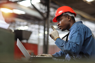 Engineer or worker man in protective uniform sitting and using computer while pose thinking something and controlling work with hardhat and electric cable line at heavy industry manufacturing factory
