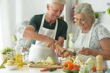 Beautiful elderly couple preparing salad in the kitchen
