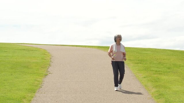 公園でウォーキング・有酸素運動する高齢者女性
