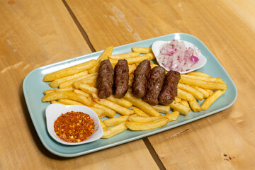 Kebabs served on a wooden board with french fries and onion