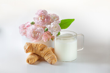 Homemade croissants and glass of milk on white table with soft pink flowers. Sweet pastry, close-up, concept of romantic Breakfast