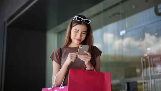 Happiness Beautiful woman enjoy shopping with smartphone , shopping bag at fashion mall. Trendy female shopping at clothes store. Smiling Woman enjoying lifestyle fashion. Shopping mall concept.