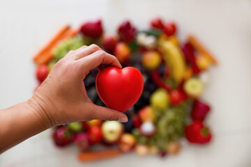 Serce trzymane w dłoniach na tle różnokolorowych owoców, dbanie o zdrowie, dieta złożona ze...
