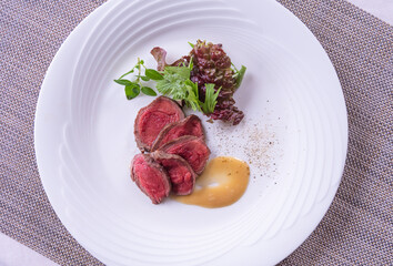 網目状のテーブルマットの上の白い皿に盛りつけた牛肉のロースト。