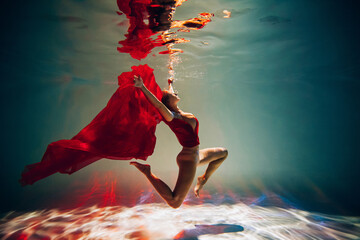 Art work. A slender, tanned girl with an athletic figure and blond hair, with red material and light underwear, in a ballet pose underwater in the pool. Aesthetic image for your design or decoration.