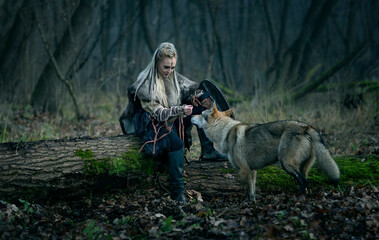 Viking woman with sword in a traditional warrior clothes with a dog-wolf in the woods - Movie and...