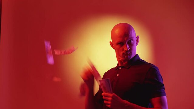 Money spender. Rich man. Success demonstration. Strange grimacing guy spreading hip of cash dollars on red yellow neon light background.