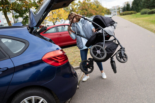 a young woman loads a stroller into the trunk of a car