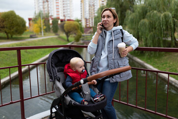 young woman talking on the phone while walking next to the stroller in which the baby is sitting