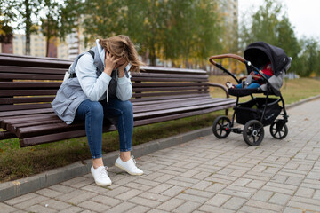 a young mother sits on a bench upset next to a baby stroller, Concept of postpartum depression - obrazy, fototapety, plakaty