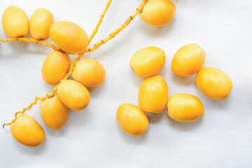 Fresh yellow dates on white wooden floor, top view.