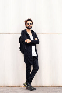 vertical photo of a beautiful young man with sunglasses leaning in a white wall, concept of urban lifestyle and stylish clothing, copy space for text