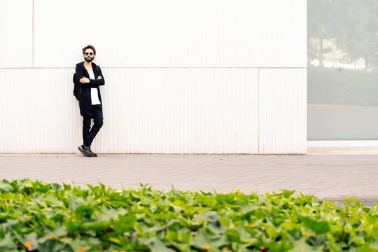 young man with sunglasses leaning in a white wall of a city park, concept of urban lifestyle and stylish clothing, copy space for text