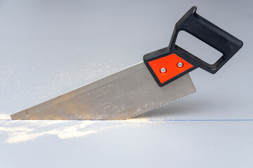 A hacksaw with a plastic handle saws a gray wooden slab, fine sawdust lying there.
