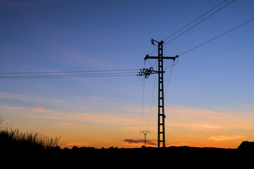 Silhouette of an electric pole on dusk background. Sunset over the electric power lines. Clean energy. High voltage electric power tower. 
