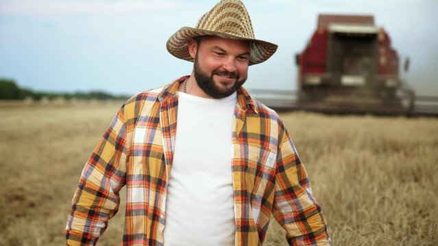 Farmer man in hat walks through wheat field and touches ripe wheat ears with his hands, controlling and checking quality. Summer harvest season. Agronomist specialist is engaged in growing plants.