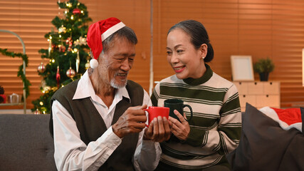 Happy senior couple celebrating Christmas together at home lighted with soft lights and candles. Holidays and people concept