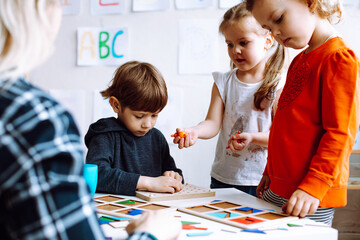 Cute, adorable little boy and two girls help do logic exercise with figures and shapes in class...
