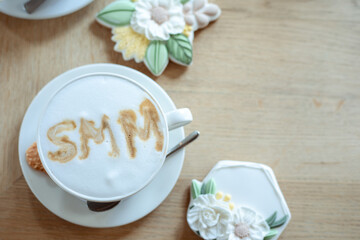Photo top view of cup of hot flavored coffee with white foam and nice icing cookies on table, free copy space, wooden background. Social media marketing, SMM, promotion, sweet desserts and drinks