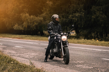 male motorcyclist in a warm jacket and helmet in cold autumn weather on the road with a motorcycle cafe racer