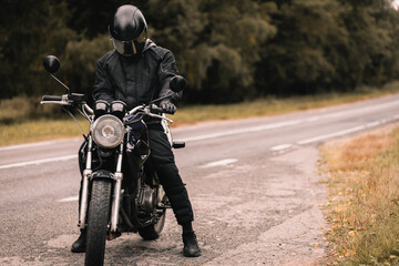 male biker motorcyclist holding a smartphone in gloves in autumn on a motorcycle cafe racer on a journey.