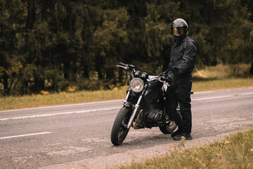 male motorcyclist in a warm jacket and helmet in cold autumn weather on the road with a motorcycle cafe racer