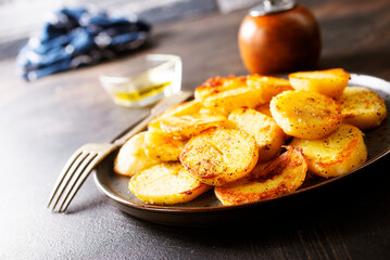 Fried potato wedges with oil, herbs on stone board