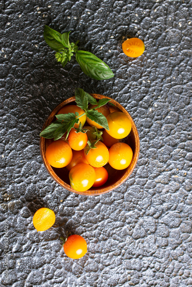 Poster Yellow ripe tomatoes in a wooden bowl on a stone background