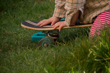 Little child is riding a skateboard backwards in the green grass