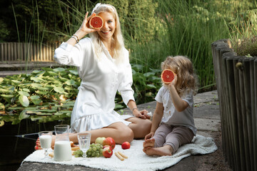 Mysterious, positive blonde woman and little girl holding grapefruits near face like eyes on...