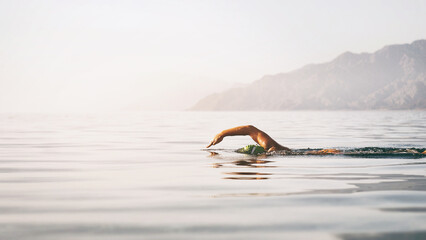 Professional swimmer woman swimming open water at sunrise sea
