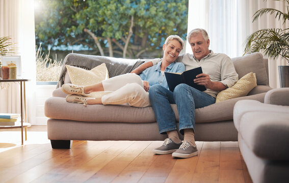 Retirement senior couple with photo album book on sofa together in summer house for vacation holiday. Happy elderly woman or people relax on couch in living room reading, talking of marriage history