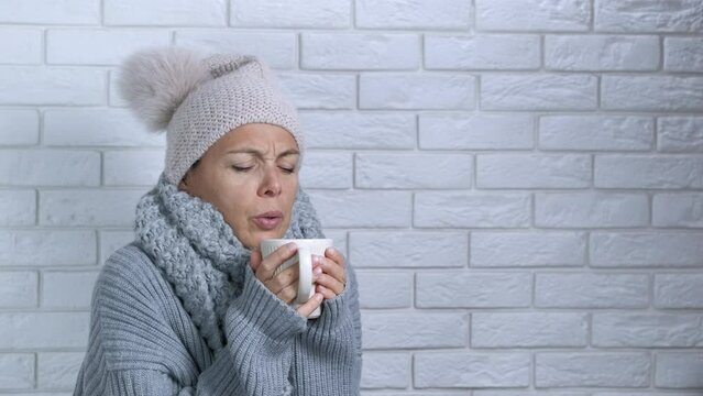 Lady feeling discomfort in clothes indoor. A young lady in winter cap try to get warm with hot bevarage in cold apartment. A concept of household debts and rising prices for heating in Europe.