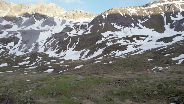 Aerial drone footage flying forward and close to an alpine meadow in a dramatic, jagged mountain landscape with residual patches of snow and alpine meadows in Switzerland.