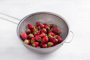 Metal colander with washed organic strawberries on a light gray table - obrazy, fototapety, plakaty