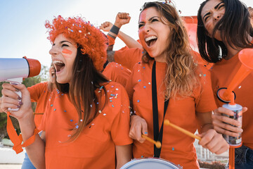 Orange sport fans screaming while supporting their team out of the stadium - Focus on left girl face