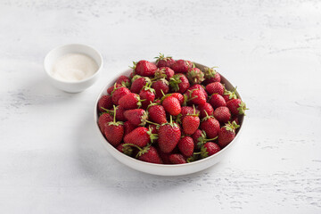 Glass bowl with ripe strawberries and sugar on a light blue background