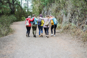 Multiracial women having fun during trekking day in mountain forest - Focus on backpacks
