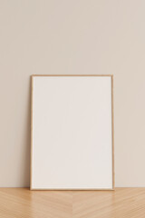 Clean and minimalist front view vertical wooden photo or poster frame mockup leaning against wall on wooden floor. 3d rendering.