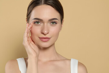 Young woman applying cream under eyes on beige background, space for text