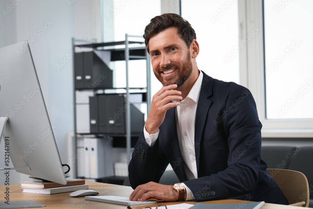Poster smiling bearded man near computer at table in office